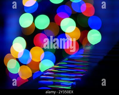 Blurred bokeh Christmas lights reflected in piano keys. Christmas and New Year celebration concept. Background wallpaper, banner. Stock Photo