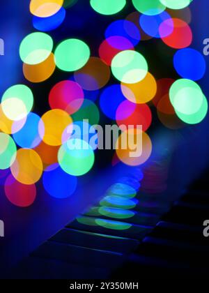 Blurred bokeh Christmas lights reflected in piano keys. Christmas and New Year celebration concept. Background wallpaper, banner. Stock Photo