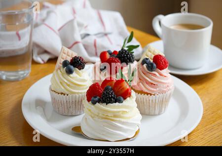 Cupcakes and mini pavlova cakes decorated with fresh berries and white chocolate Stock Photo