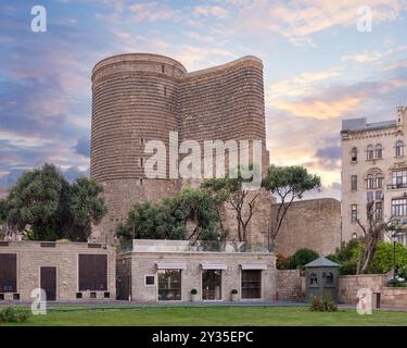 The Maidan Tower in Baku, Azerbaijan stands tall against a backdrop of clouds in the evening sky, with lush greenery surrounding the historic building Stock Photo