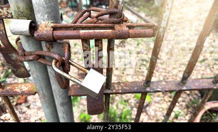 Shiny silver metal lock pad hooks onto an old, rusty chain, capturing the contrast between new and aged metal, symbolizing security, access, and the p Stock Photo