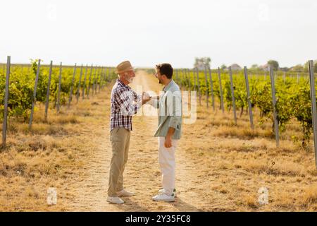 Two men share a meaningful discussion amidst rows of grapevines, enjoying the warmth of the late afternoon sun, symbolizing connection and tradition i Stock Photo