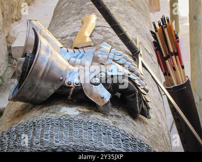 A knight in shining steel armor and leather gloves stands ready for battle, with a wooden shield and iron equipment offering protection. Stock Photo