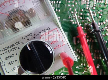 Electronic circuit testing. Electrical measuring instruments. Analog multimeter on the soldered electronic surface. Focused on the dial plate. Stock Photo