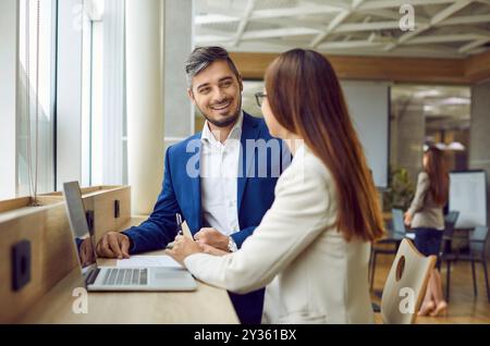 Smiling young coworkers discussing work project in office sitting with laptop. Stock Photo
