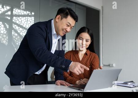 Asian business team working together on project showing teamwork and collaboration. Man and woman using laptop in modern office environment, discussing ideas and solutions. Stock Photo