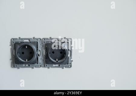 Two empty electrical outlets are installed on a plain white wall, awaiting connection and installation in a new building project Stock Photo