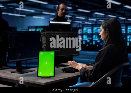 Engineer in data center uses isolated screen tablet to update systems, protecting servers from software vulnerabilities. IT expert uses chroma key device to look for errors affecting servers Stock Photo