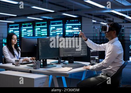 Team of engineers immersed in virtual reality in server farm, doing units maintenance. IT experts coworkers using VR headset to optimize servers performance, checking operations in data center Stock Photo