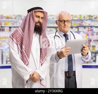 Doctor and a saudi arab man looking at a digital tablet inside a pharmacy Stock Photo