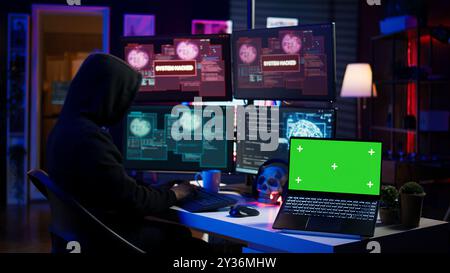 Hacker doing computer sabotage using trojan ransomware on green screen laptop. Cybercriminal uses mockup device to demand ransom money from victims in exchange for access to their data, camera B Stock Photo
