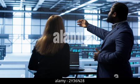 Team of engineers in data center doing brainstorming and running error checking utilities to fix problems. Teamworking colleagues in server hub looking for network issues affecting rigs, camera A Stock Photo