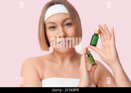 Beautiful mature woman with bottles of essential oil on color background, closeup Stock Photo