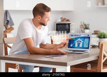 Young man with smart home application on gadgets in kitchen Stock Photo