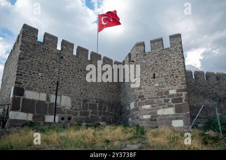 Ancient Ankara Castle's stone walls rise against cloudy sky, Turkish flag proudly waves atop battlements. Turkey Stock Photo