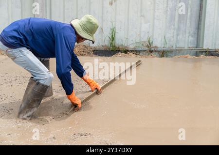 Worker plastering wet concrete surface after pouring concrete floor in construction site. Stock Photo
