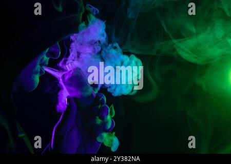 male vaper holding vape electronic cigarette close-up on background of colored smoke, concept of harm of smoking Stock Photo