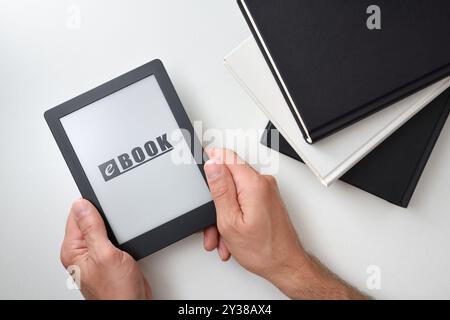 Background with hands holding an ebook on white table with traditional paper books stacked. Top view Stock Photo