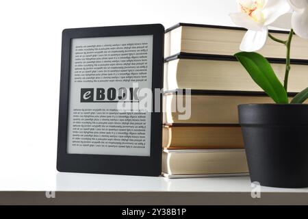 Digital reading concept with ebook on white bookshelf resting on traditional paper books and decoration screen with white isolated background. Front v Stock Photo