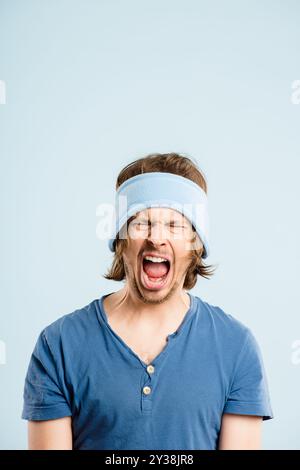 Man, angry and shouting in studio, mental health and stress for pain on blue background. Male person, screaming and frustrated for information, yell Stock Photo