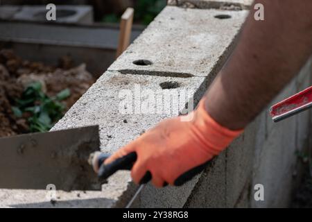 A bricklayer works on blocks to build a wall on a construction site with concrete, a trowel, a level and a grinder Stock Photo
