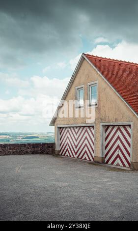 Garage in the skies. Beige two storey building with two striped garage doors. Wien of the valley and cloudy sky in the background. Stock Photo