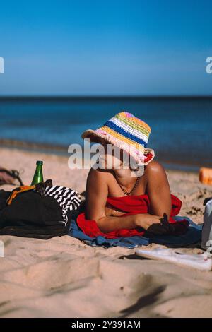 A woman in a swimsuit and a multi-colored hat rests on the beach. Stock Photo