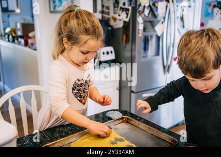 Two children cutting shapes from cookie dough on a baking tray Stock Photo