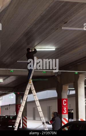 City Worker electrician repairs LCD lamp on mall parking. Maintenance of electrical networks of a shopping center or a manufacturing enterprise. Stock Photo