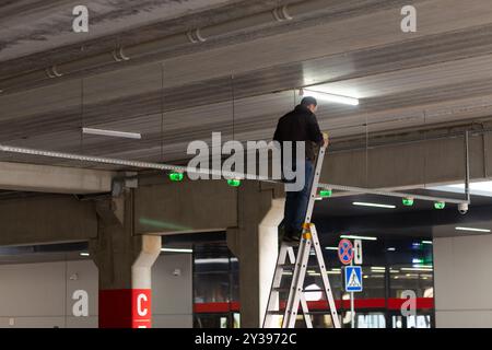 City Worker electrician repairs LCD lamp on mall parking. Maintenance of electrical networks of a shopping center or a manufacturing enterprise. Stock Photo