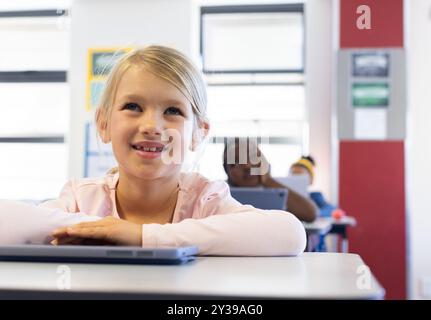 In school, girl smiling and using laptop in classroom, focusing on lesson Stock Photo