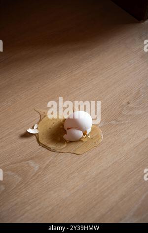 A cracked raw egg that was dropped by mistake on the wooden kitchen floor. Top view, close up, no people. Stock Photo