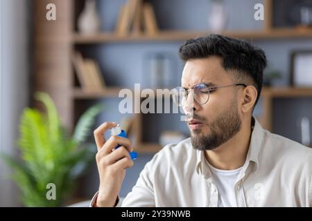 Close-up photo of a young Indian man at home, holding an inhaler and suffering from an asthma attack and allergies. Stock Photo
