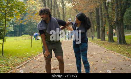 Outdoors in nature park Indian Arabian couple friends man woman stop after cardio fast run jog running man tired exhausted resting feel bad unwell Stock Photo