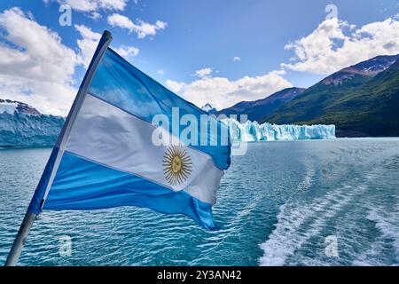 Argentinian flag waving by a picturesque lake with stunning glacier views and mountainous landscape on a sunny day. Stock Photo