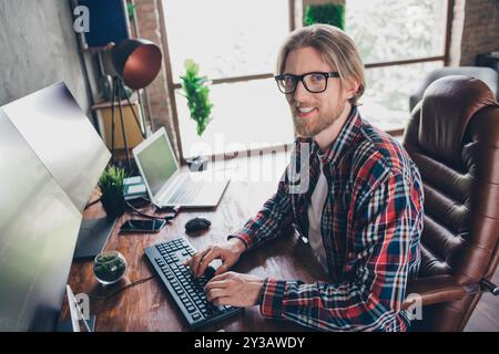 Photo system administrator young blond hair guy at loft design modern office in front of computer coding using keyboard and modern monitors Stock Photo