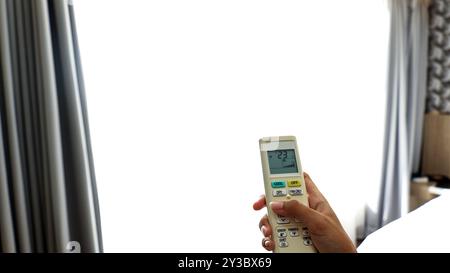 Woman Operating Remote Controller on Air Conditioner Inside the Room, Female Hand with AC Remote Control Stock Photo