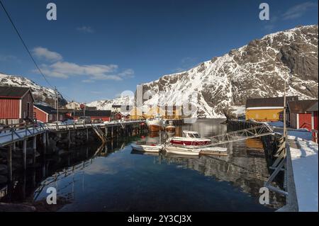 Fishing village with yellow and red houses in front of snow-covered mountains, Nusfjord, Flakstadoya or Flakstadoy, Vestvagoya island, Lofoten, Nor Stock Photo