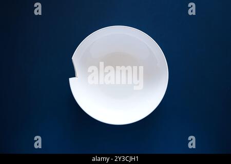Broken or chipped white ceramic soup plate on a dark blue background, top view, no people Stock Photo