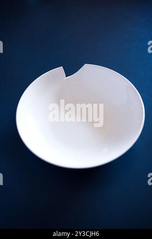 Broken or chipped white ceramic soup plate on a dark blue background, top view, no people Stock Photo