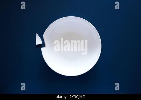 Broken or chipped white ceramic soup plate on a dark blue background, top view, no people Stock Photo