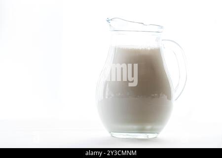 Sunlit Crystal Jug Filled with Milk, isolated on White Background. Stock Photo