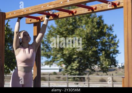 Woman exercising while hanging from one bar to another in an outdoor gym, horizontal view Stock Photo