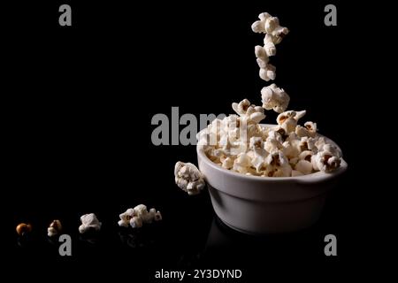 Popcorn popping in the air above a white bowl, on a shiny black background Stock Photo