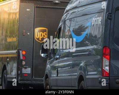 LOS ANGELES, CA - May 2024: Amazon Prime delivery van and brown UPS truck line up on residential street in West Hollywood, California Stock Photo