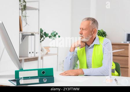 Thoughtful mature engineer with computer and wind turbine model on table in office Stock Photo