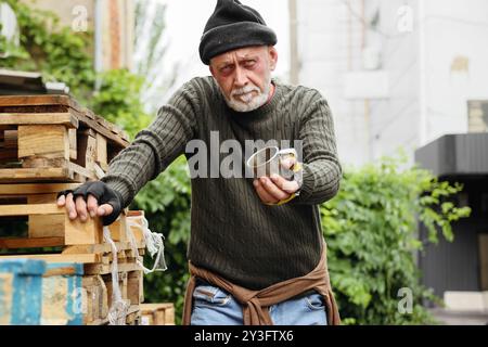 Mature homeless man with cup asking for money on street Stock Photo