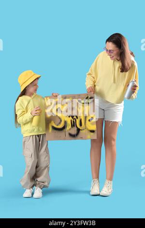 Little girl and her mother with spray paint cans holding graffiti on blue background Stock Photo