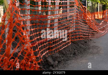Protective orange mesh fencing at a construction area, capturing the details of safety precautions on a city street. Stock Photo