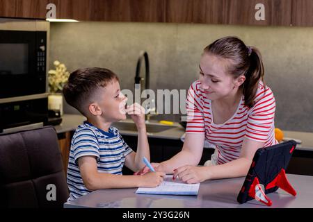 Beautiful mother helping son doing schoolwork at home. Stock Photo
